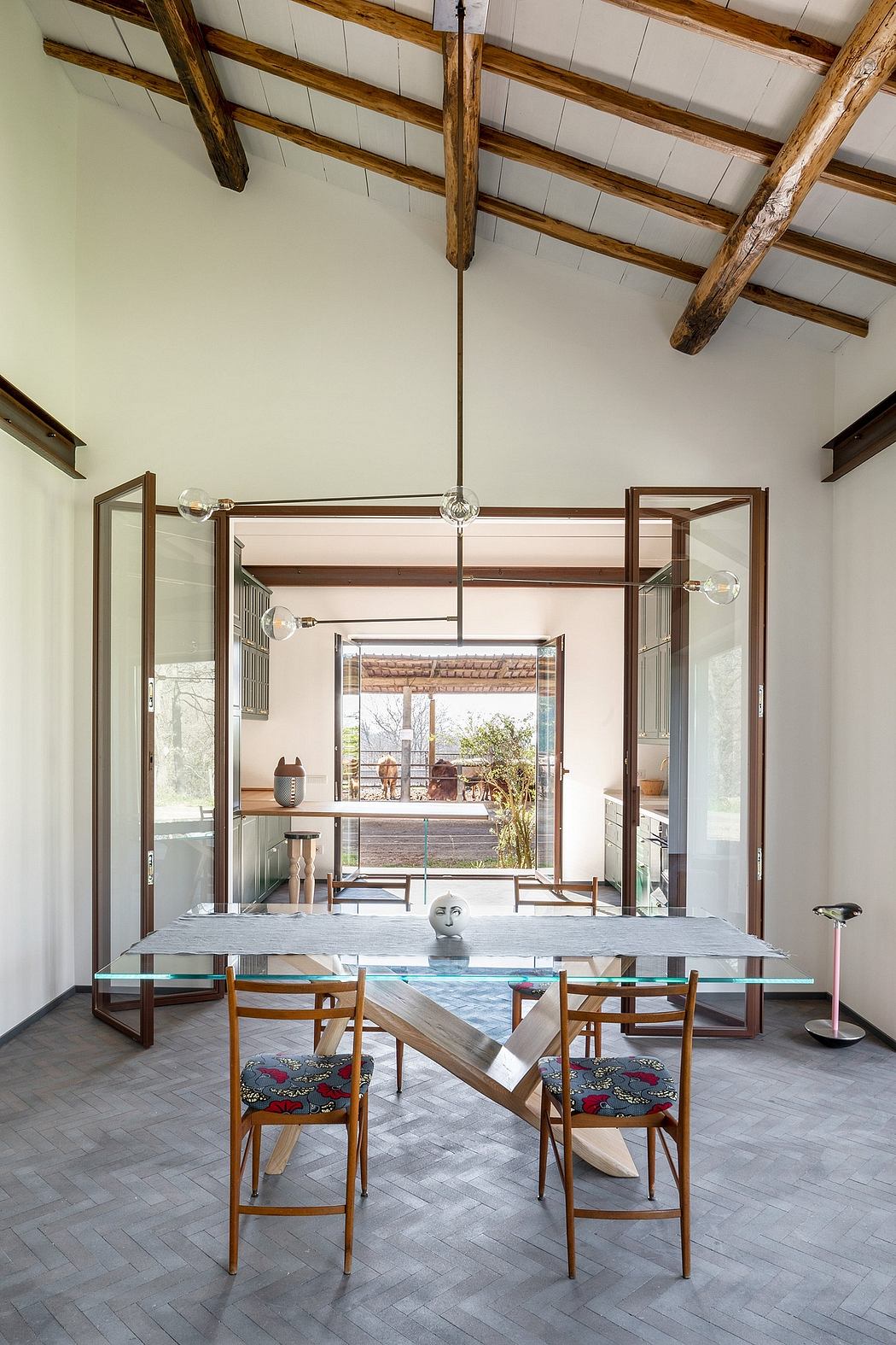 Rustic wooden beams, glass and steel table, patterned chairs, and panoramic glass doors.