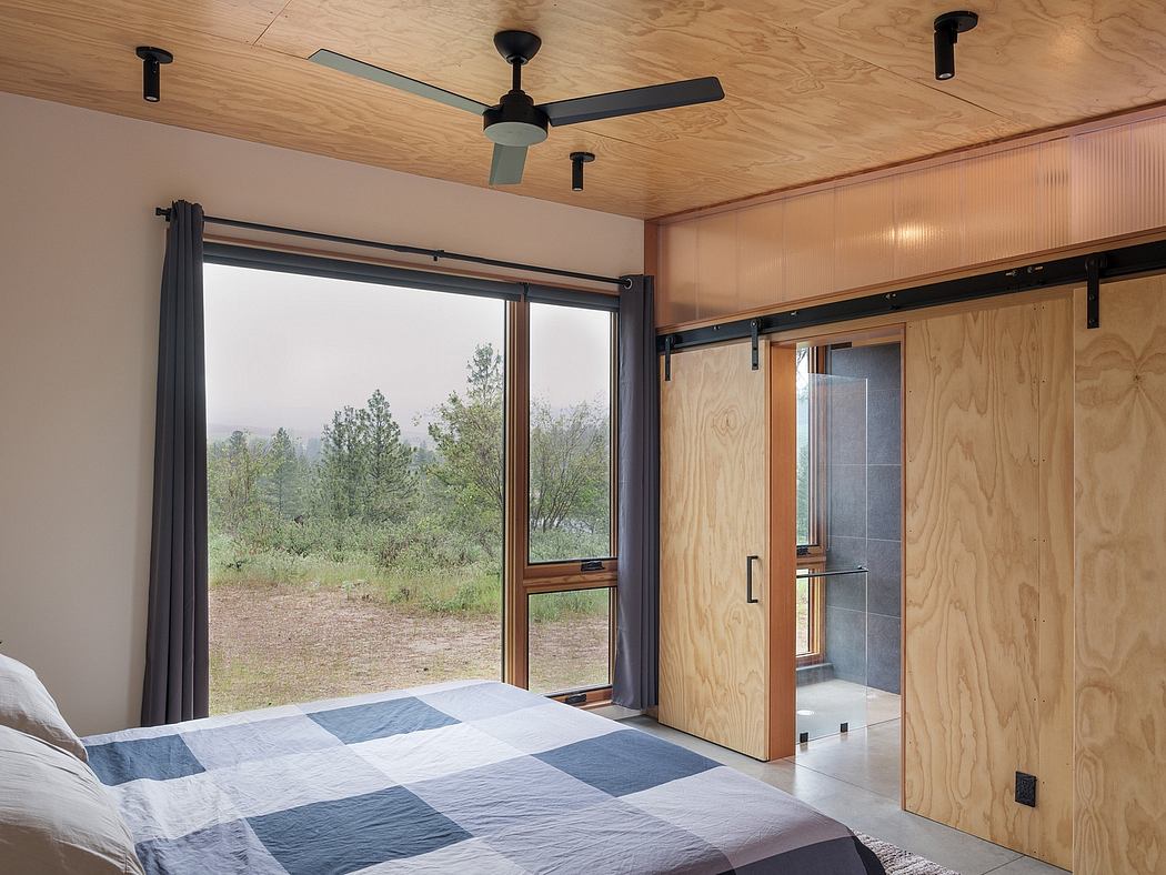Spacious bedroom with wooden walls, large windows, and sliding barn door leading to bathroom.