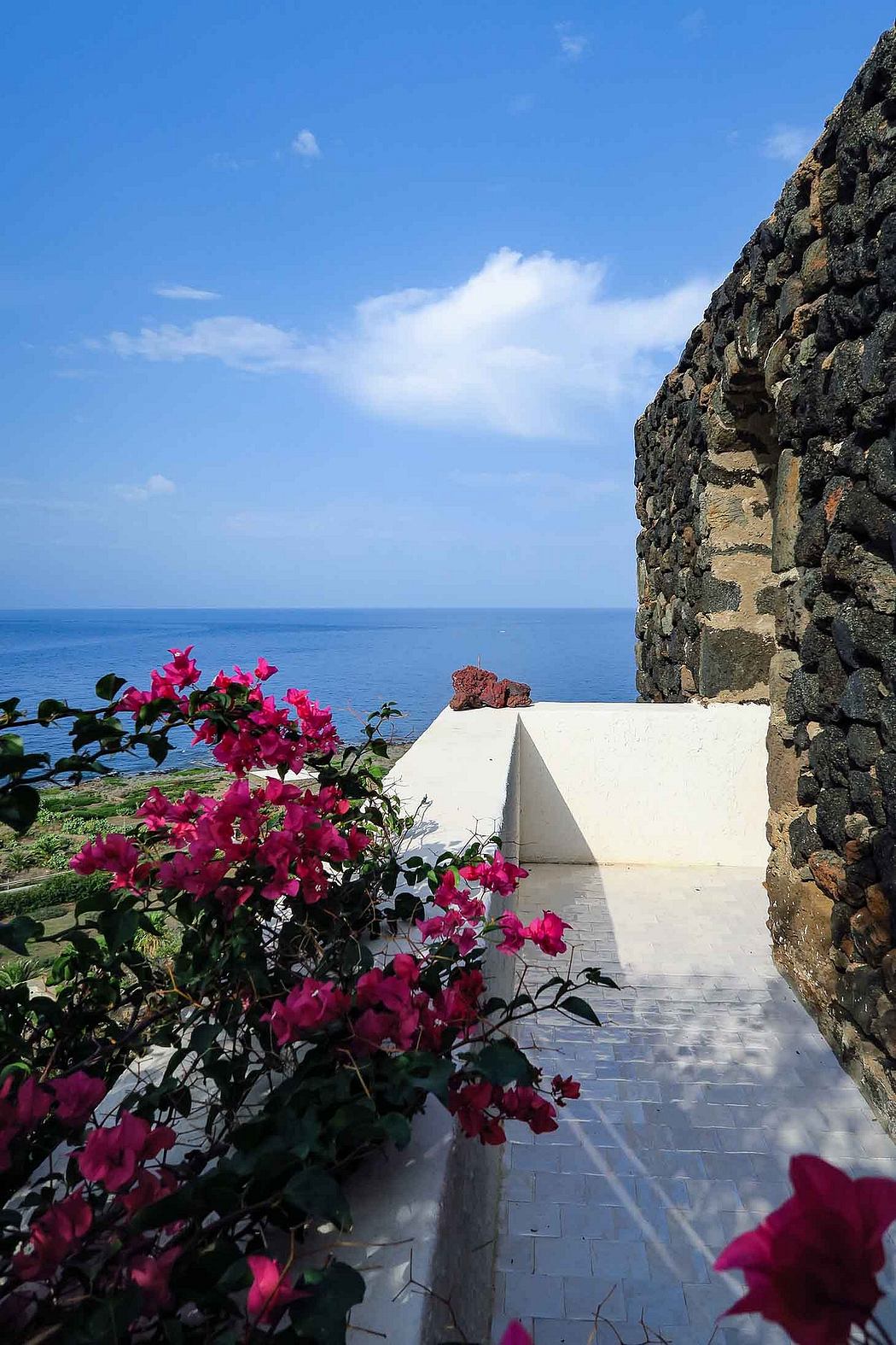 A scenic walkway framed by vibrant bougainvillea blooms, leading to a tranquil ocean vista.