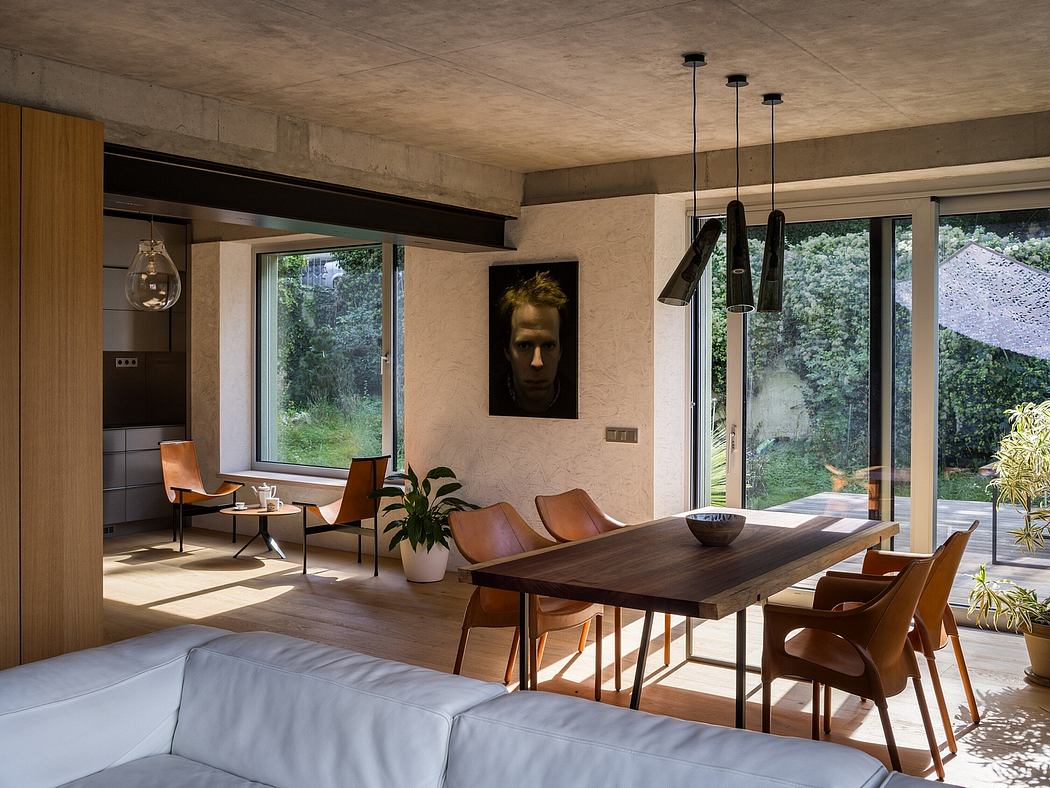 Striking modern interior with concrete ceiling, wooden dining table, and large windows overlooking lush greenery.