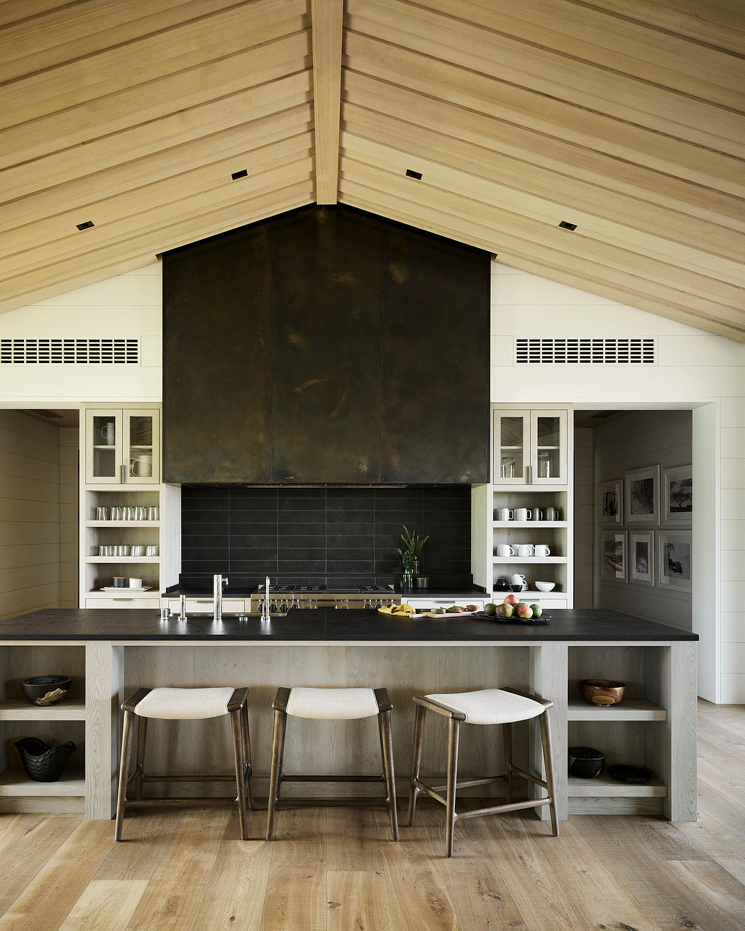Spacious kitchen with vaulted wooden ceiling, built-in shelving, and sleek black countertops.