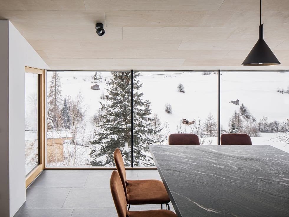 Large windows offer a scenic winter view of snowy landscape. Modern interior design with concrete table.