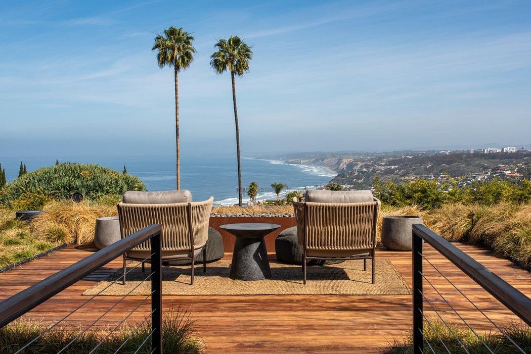 Elevated patio with woven chairs and table, overlooking scenic coastline with palm trees.
