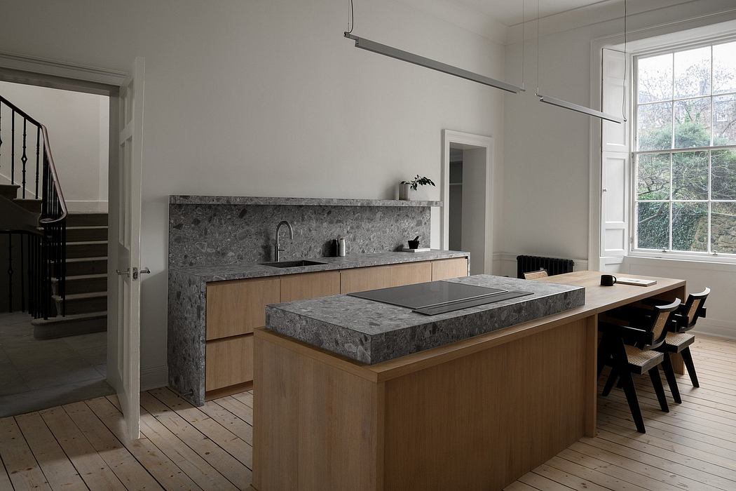 A modern, minimalist kitchen with a gray stone countertop, wooden cabinets, and a large window.