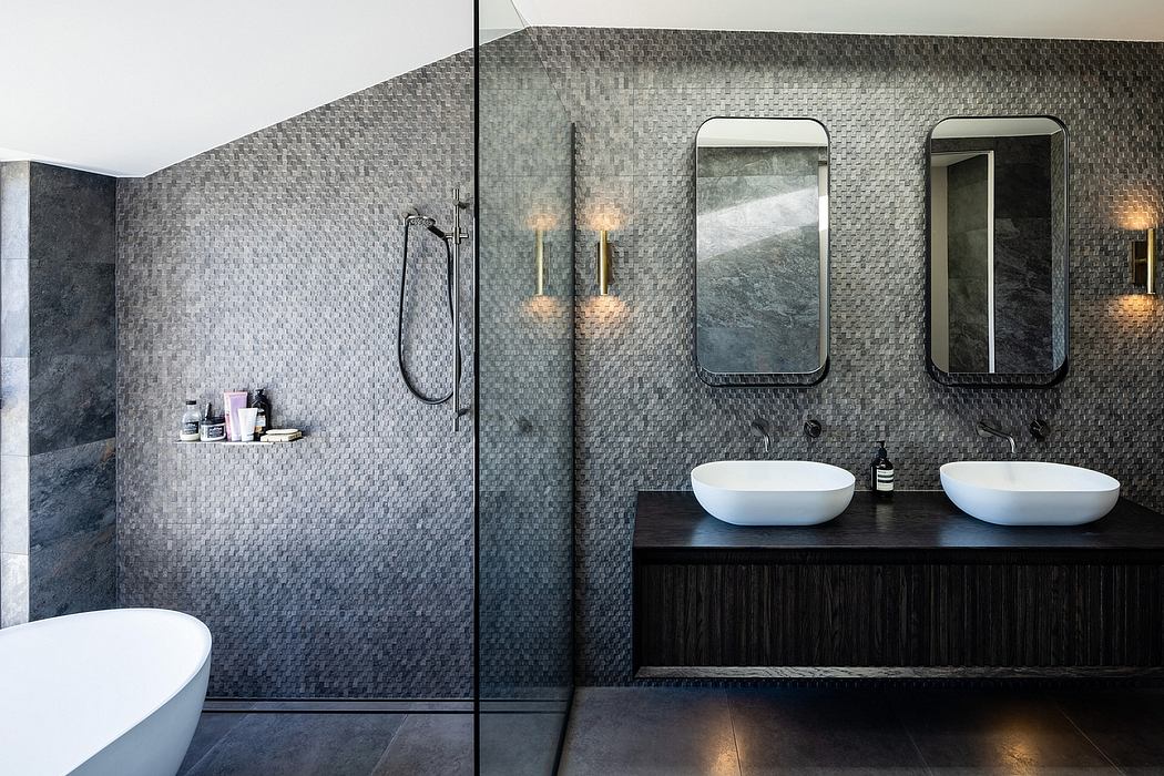Minimalist bathroom with gray tile walls, vanity with dual sinks, and wall-mounted mirrors.