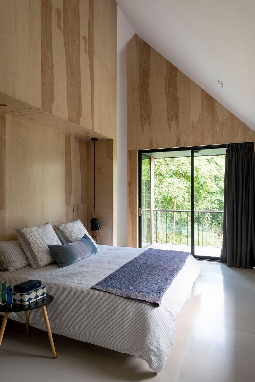 Spacious bedroom with wooden paneled walls, large window, and contemporary furnishings.