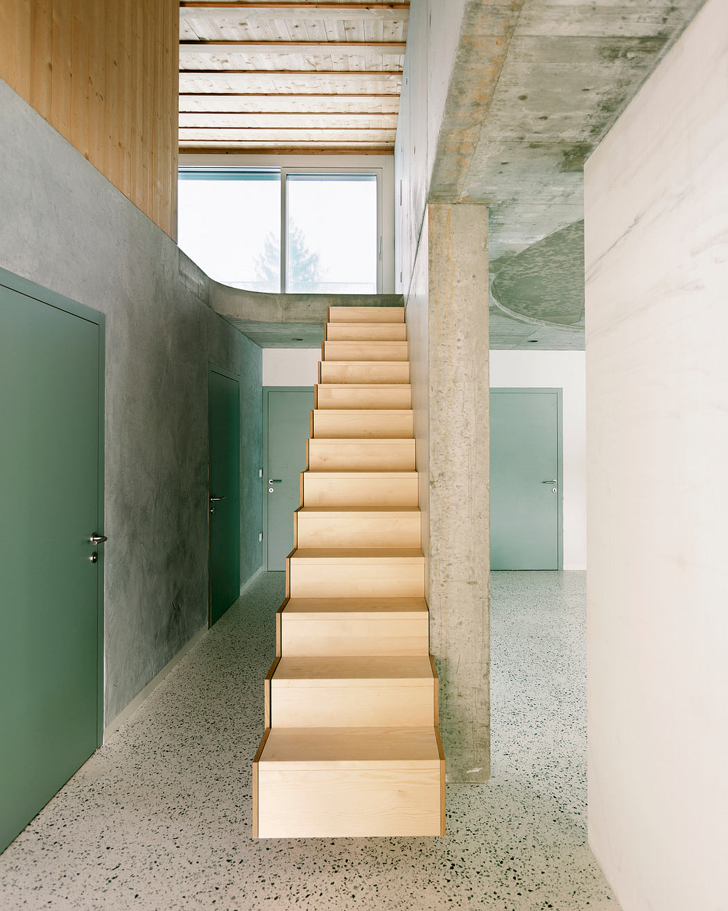 A modern staircase with wooden steps and concrete walls leading to an upper level.