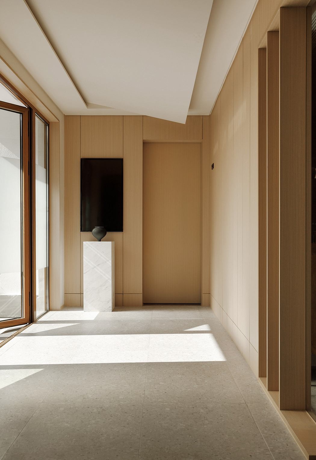 Minimalist entrance hallway with clean lines, warm wood paneling, and neutral tile flooring.