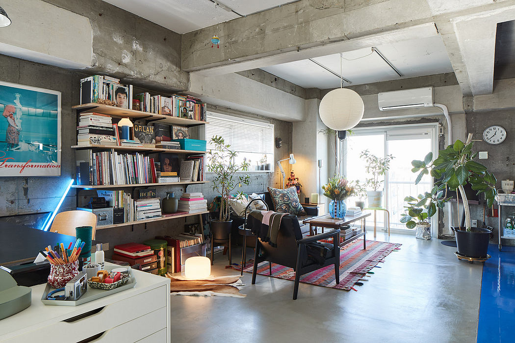 Spacious loft-style living space with concrete walls, bookshelves, and plants creating a cozy atmosphere.