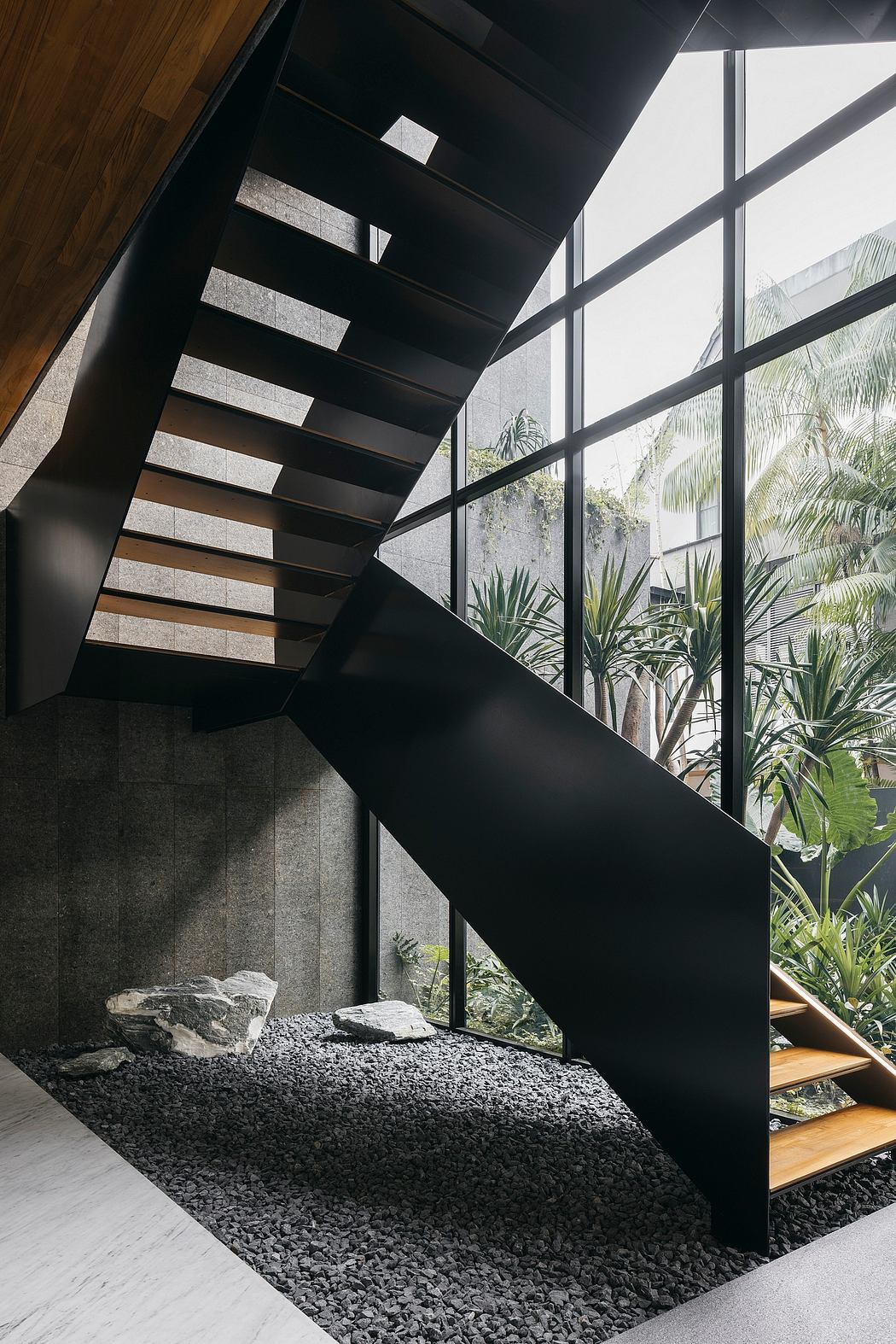 Striking staircase design with contrasting black metal and wood, surrounded by lush greenery.