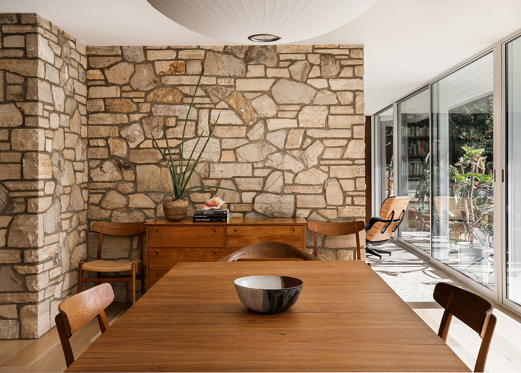 A rustic dining area with a stone wall, wooden furniture, and large windows.