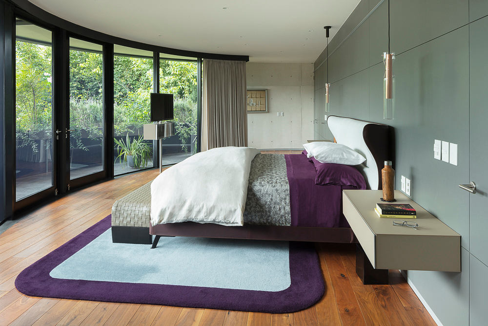 Stylish contemporary bedroom with curved windows overlooking lush greenery.