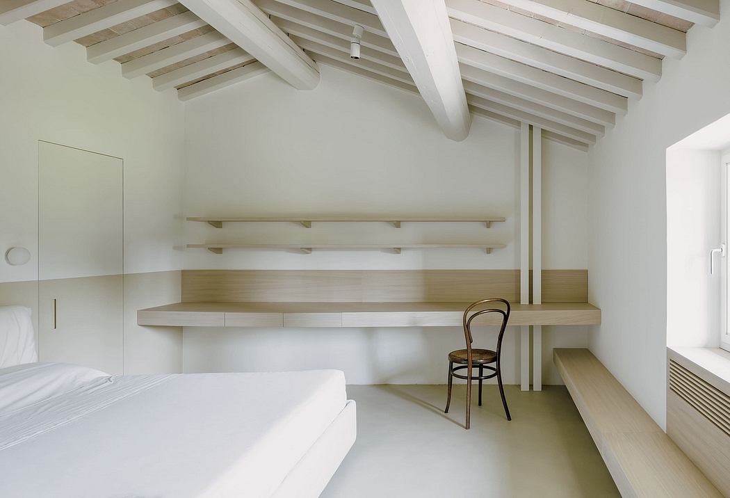 White minimalist bedroom with wooden beams, shelves, and a simple wooden chair.