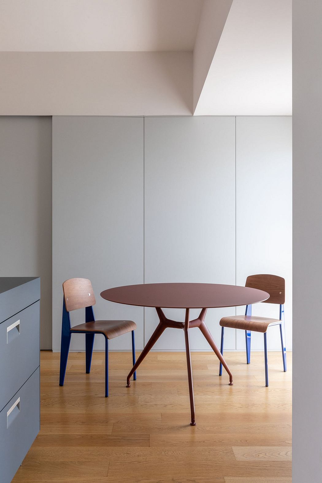 A minimalist dining area with a round wooden table and Eames-style chairs on a wooden floor.