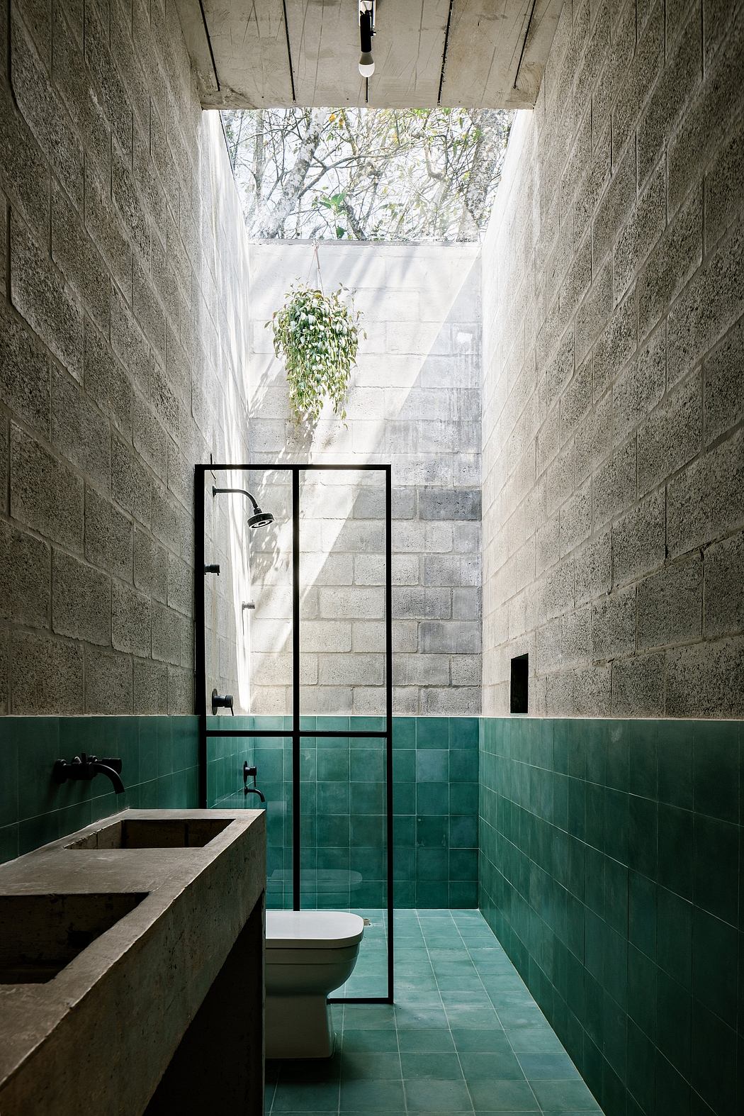 A minimalist bathroom with concrete walls, green tiles, and a large skylight providing natural light.