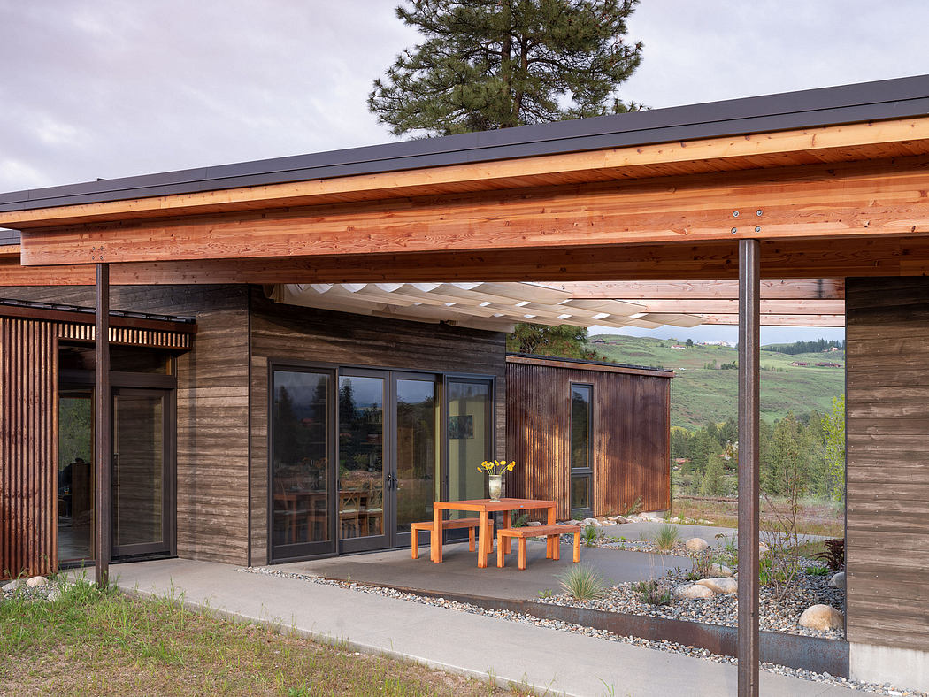 A contemporary wooden cabin with a covered patio and an orange outdoor furniture set.