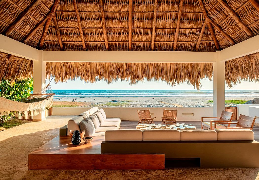 Thatched roof pavilion with luxurious beachfront seating area and panoramic ocean view.