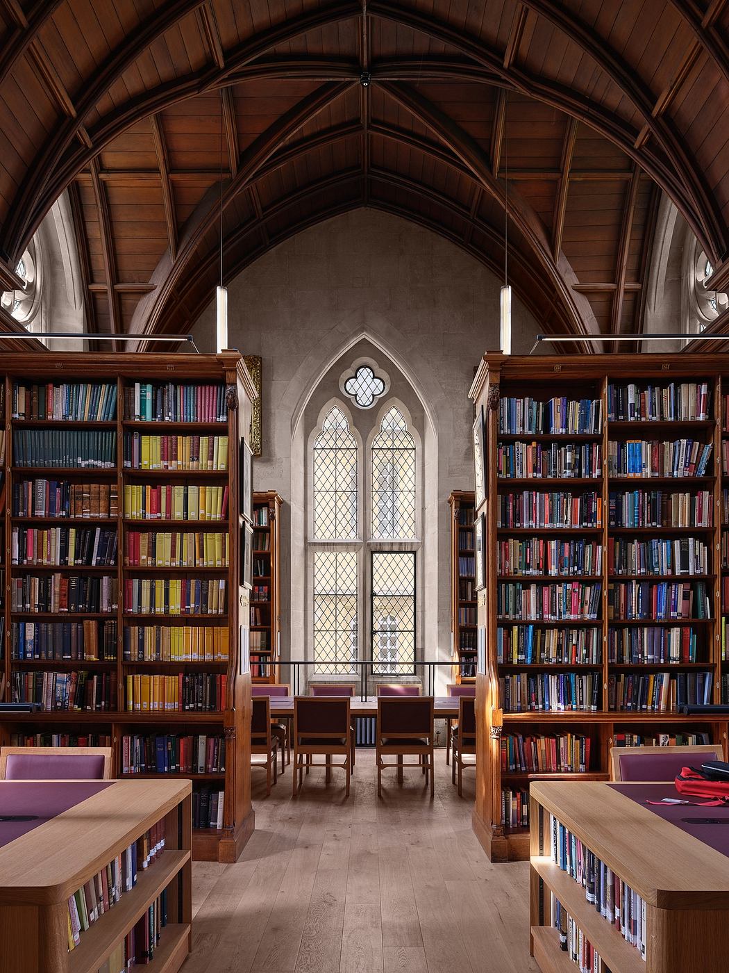 A majestic, gothic-inspired library with ornate wooden arched ceilings, stained glass windows, and rows of bookshelves.