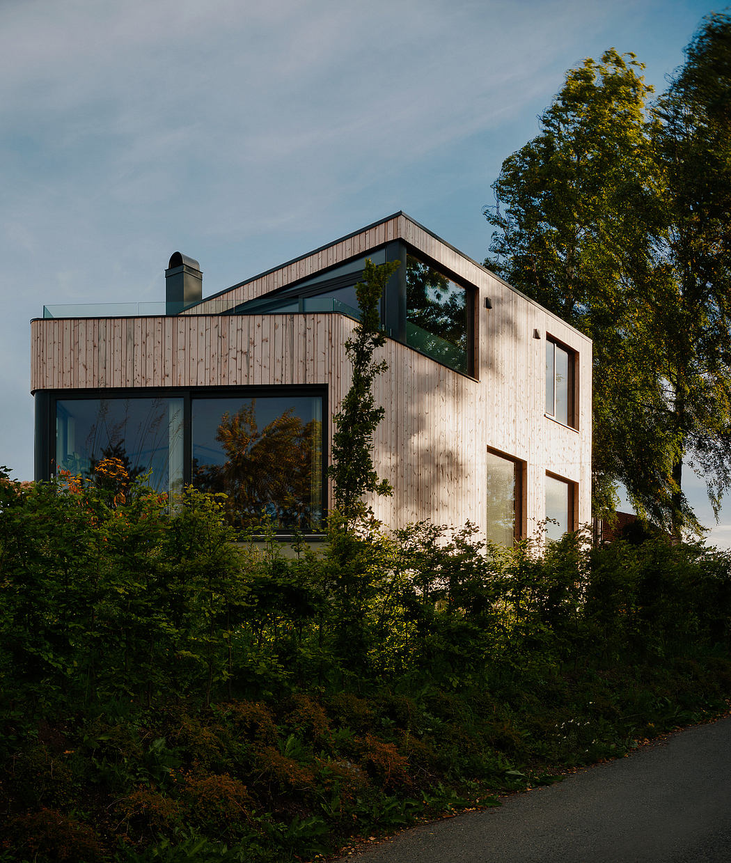 A modern wooden structure with large windows surrounded by lush greenery.