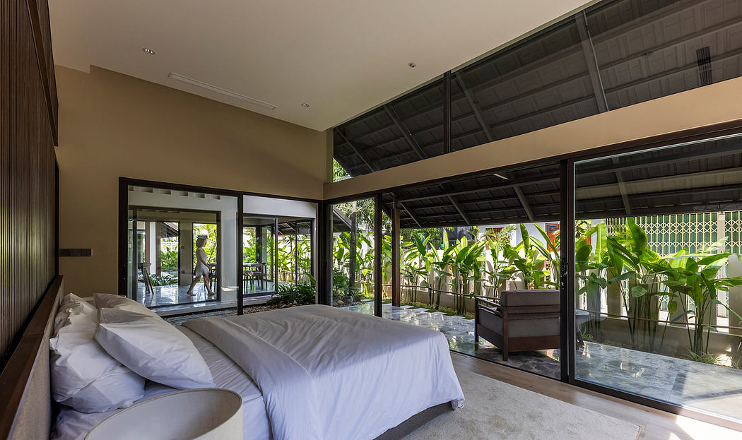 Spacious tropical bedroom with glass walls, dark wood accents, and lush greenery.