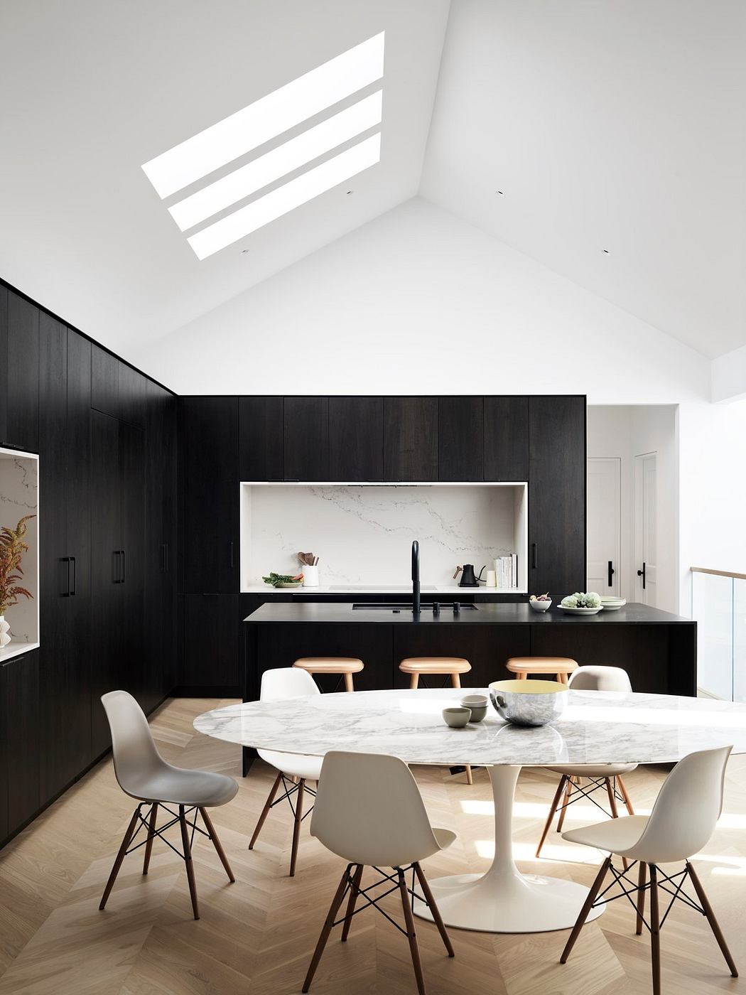 A sleek, modern kitchen and dining area with a marble-top table, black cabinetry, and skylights.