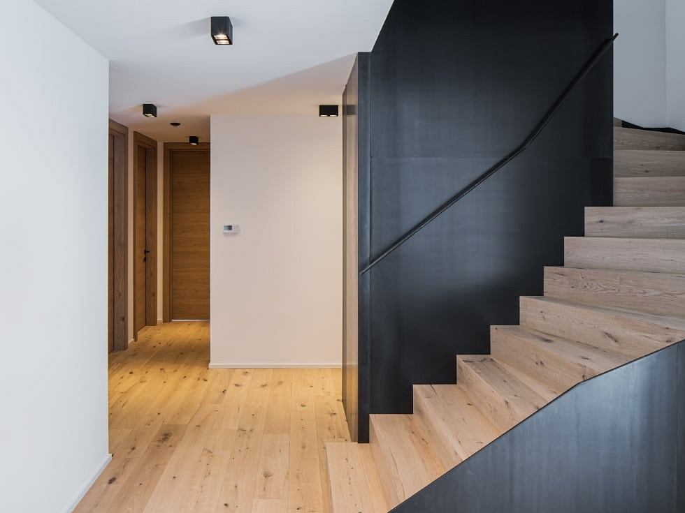 Modern staircase with black metal railing and light wood flooring leading to a doorway.