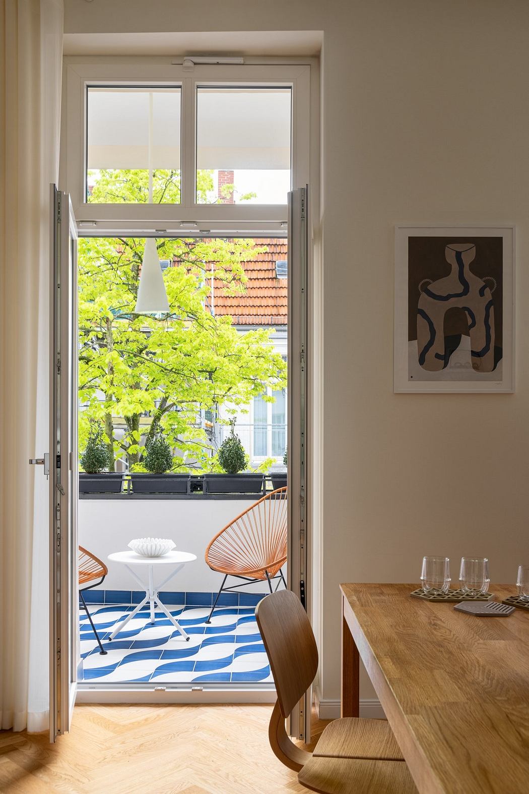 Bright modern interior with wooden furniture, abstract artwork, and green foliage outside.