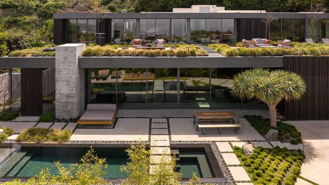 A sleek, modern home with a glass facade, terraced gardens, and a reflection pool.