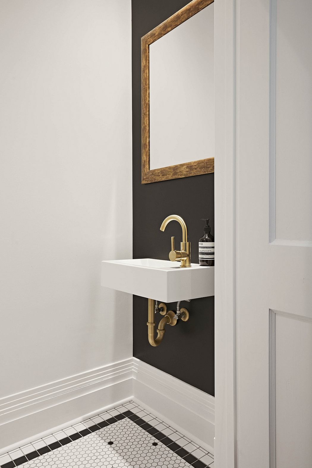 A modern minimalist bathroom with a white vanity, brass faucet, and hexagonal tile floor.