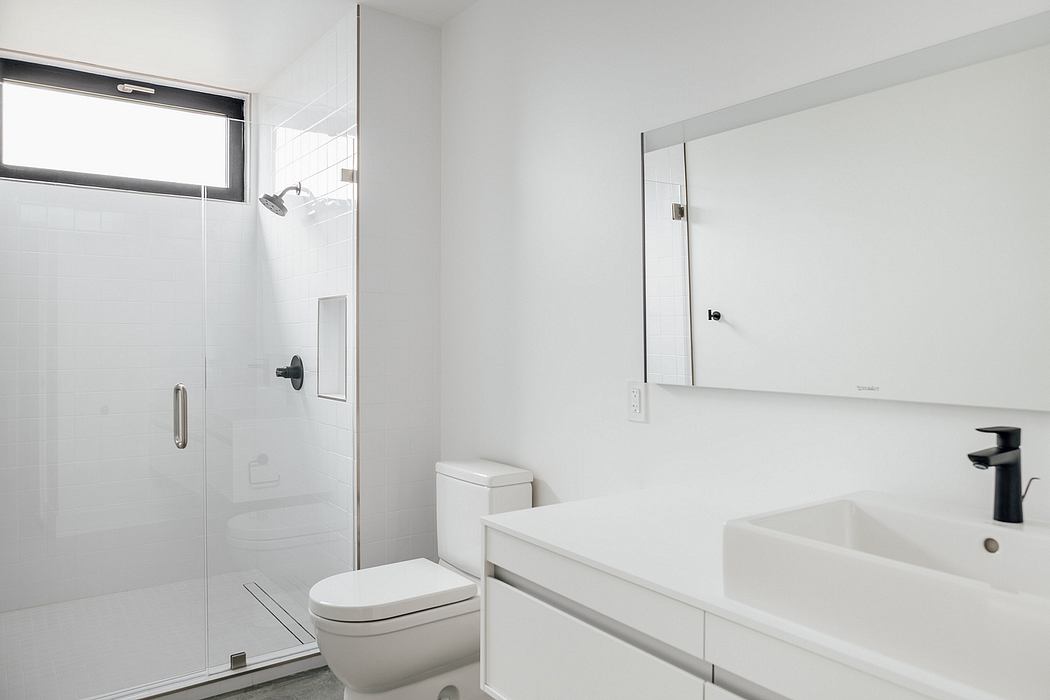A modern, minimalist bathroom with a glass shower door, vanity, and mirror.