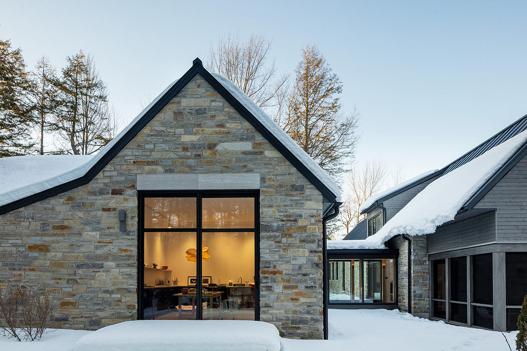 A modern stone cottage with large windows overlooking a snowy landscape.