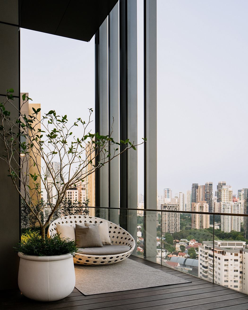 Sleek modern balcony with cozy seating, greenery, and a sweeping cityscape view.
