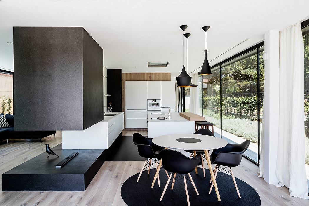 Sleek monochrome kitchen and dining area with modern lighting and large glass windows.