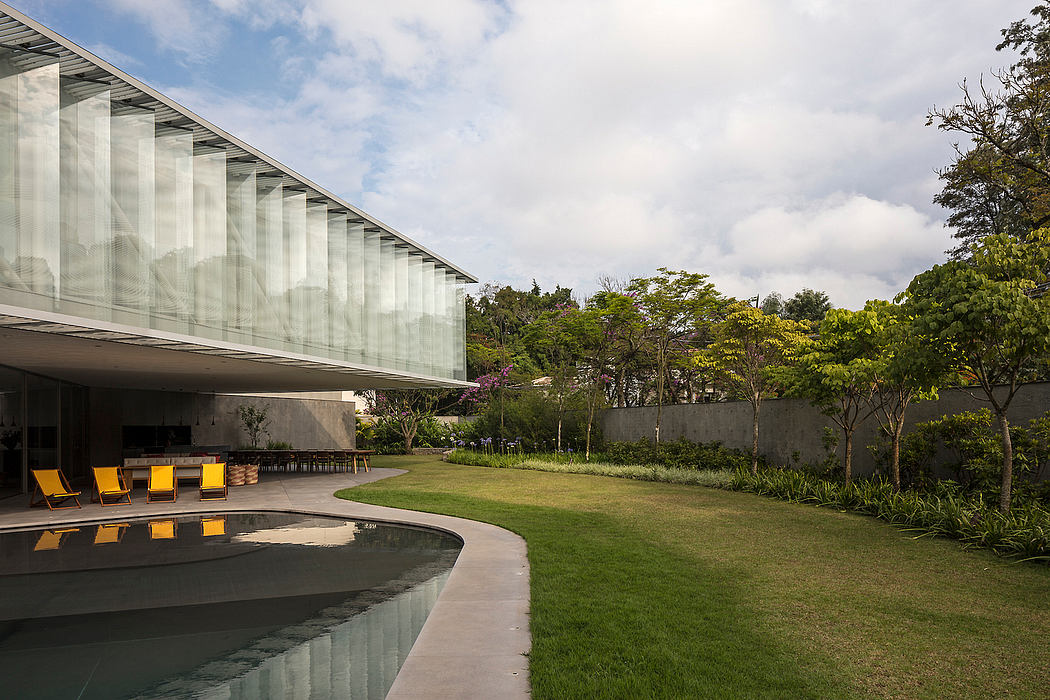 A modern glass and concrete structure surrounded by lush greenery, featuring a pool and lounge chairs.