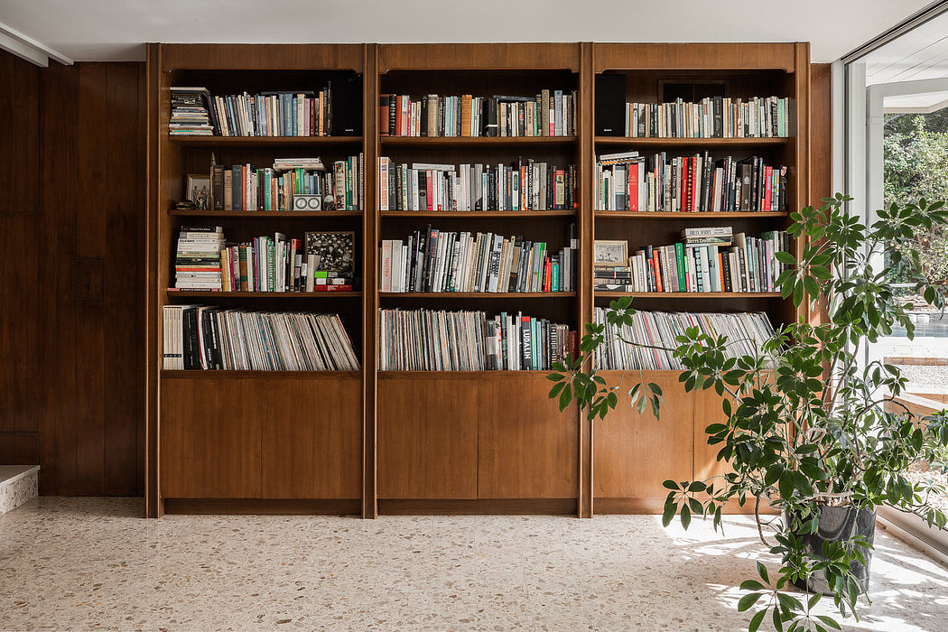 Wooden bookshelves with extensive collection, plants, and sunlit terrazzo floor.