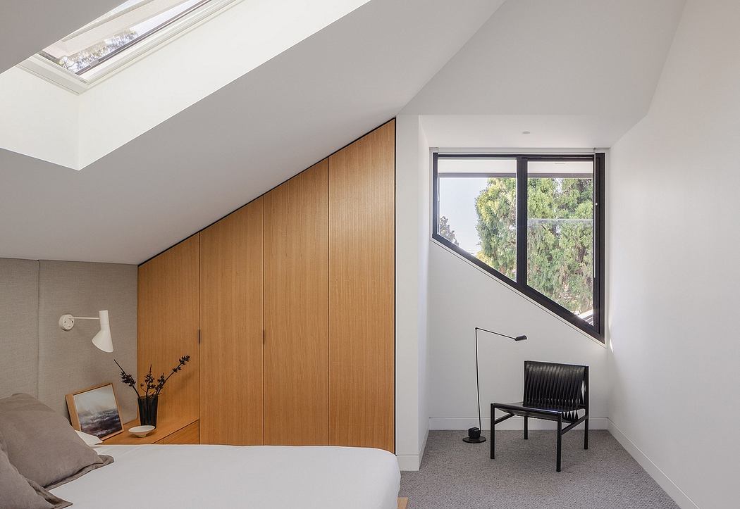 Minimalist bedroom with wooden built-in wardrobe, large window, and black accent chair.