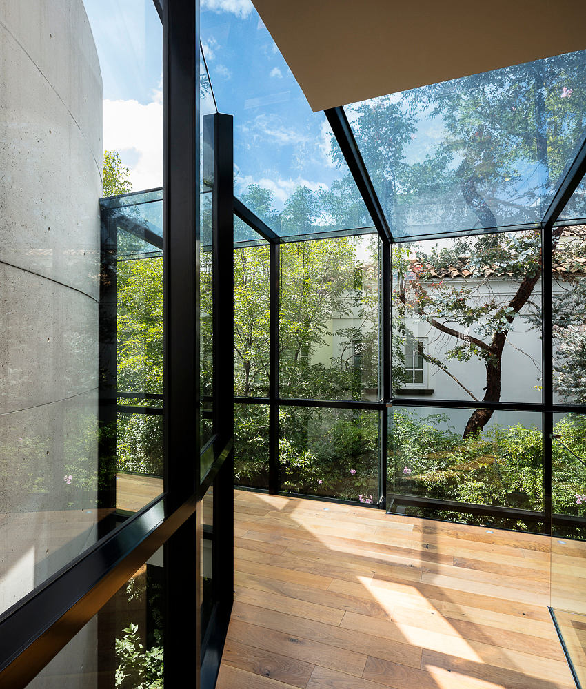 A modern glass and concrete structure with a wooden floor and lush garden views.