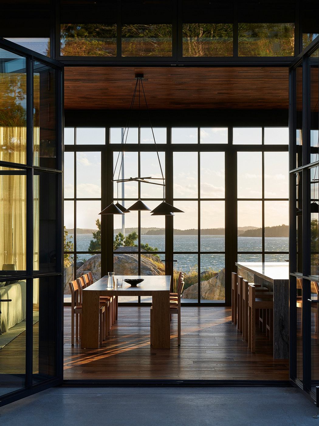 Expansive glass walls frame a breathtaking waterfront view, complemented by a modern, wood-clad interior.