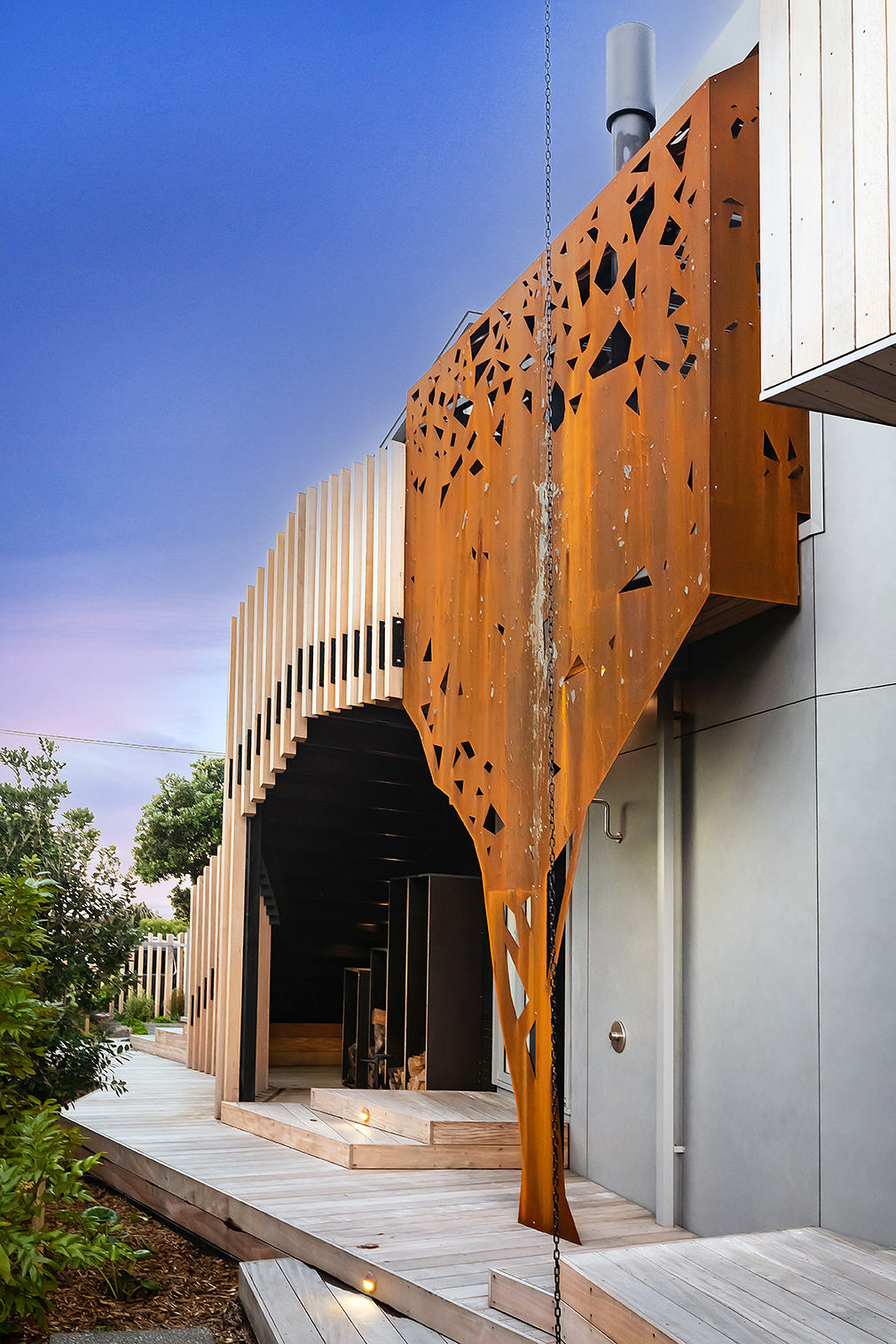 Striking architectural facade with perforated orange panels and wooden walkway leading to entrance.