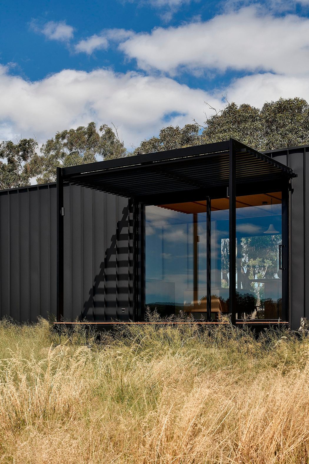 A modern, modular container home with a sleek, black exterior and large windows overlooking nature.