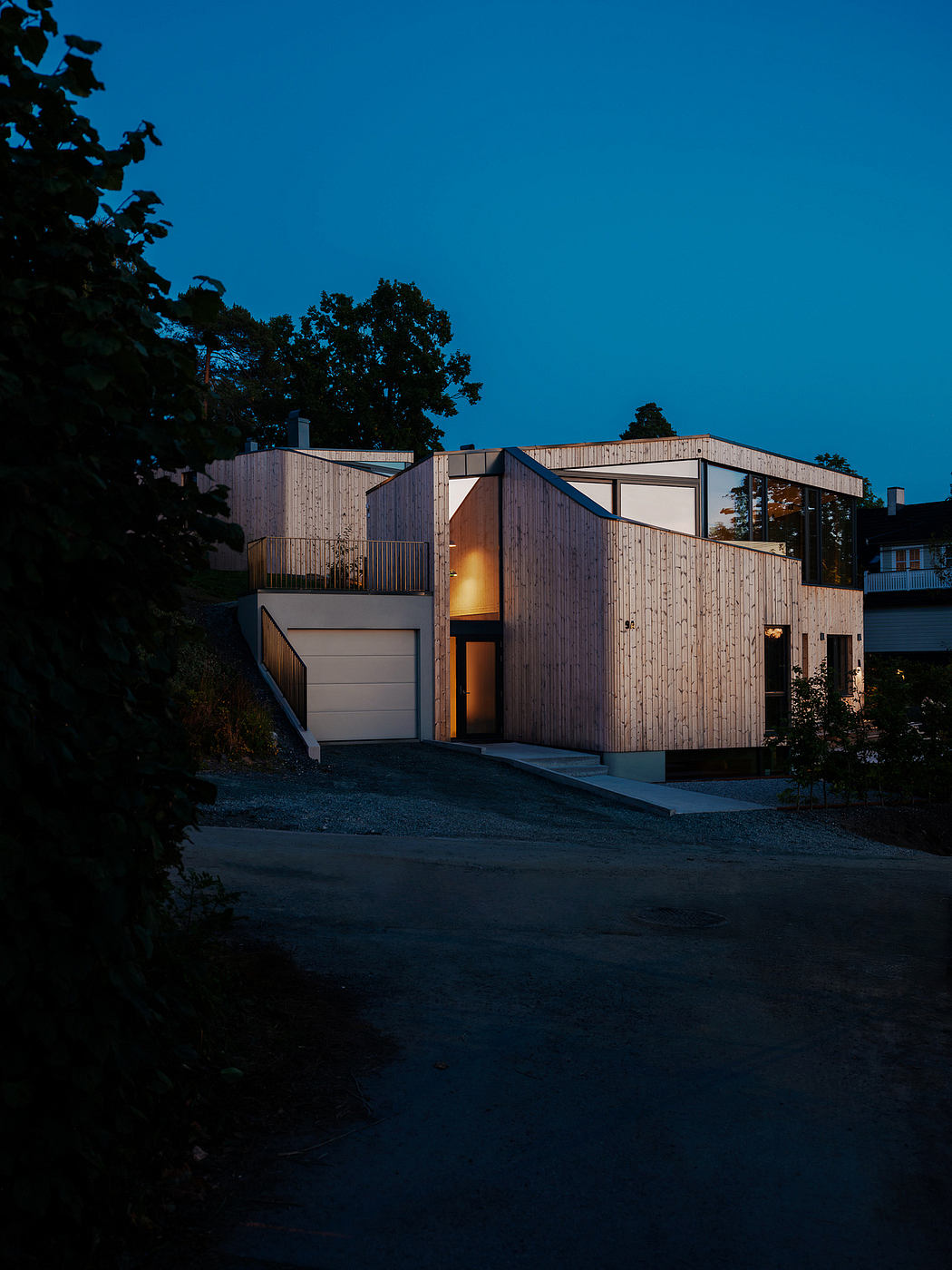 A modern wooden structure with an illuminated entryway, set against a dark blue sky.