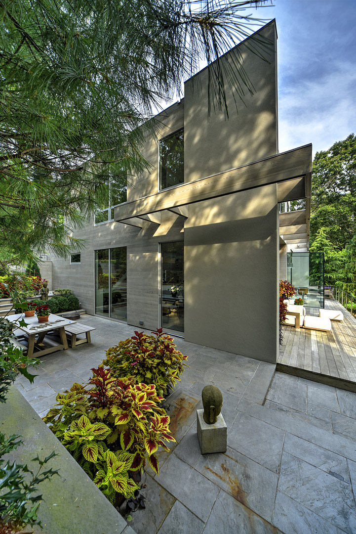 Modern architectural home with angular glass facade, stone patio, and vibrant garden.