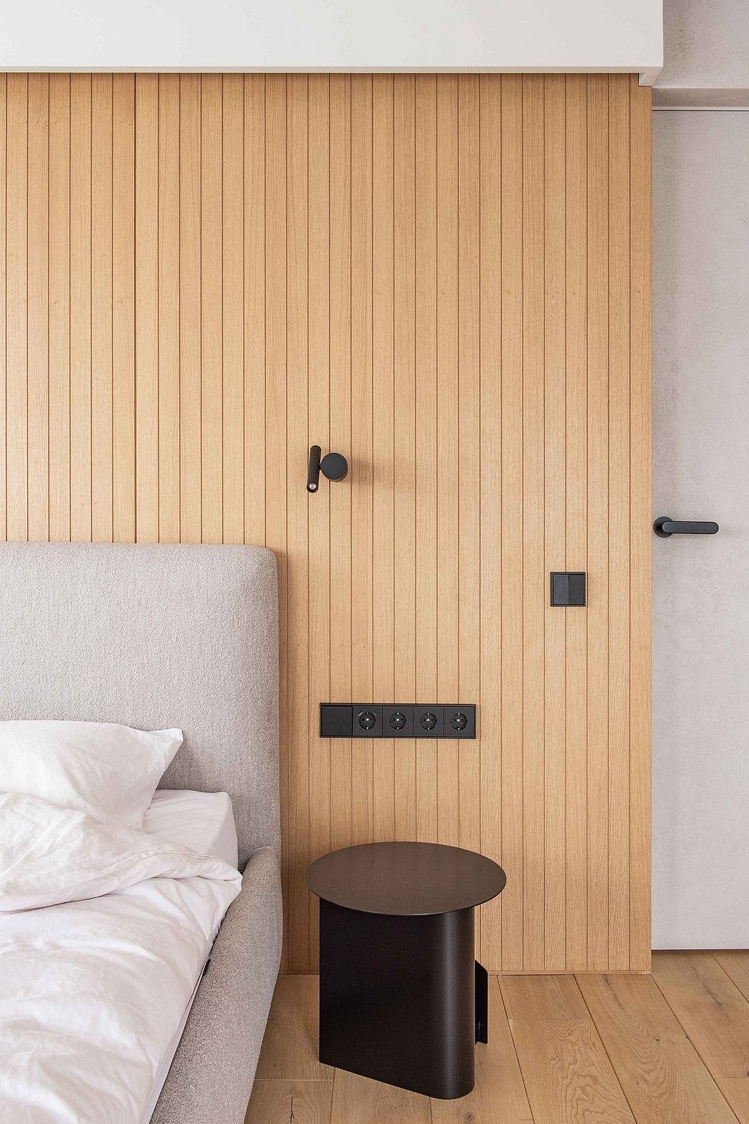Minimalist bedroom with wooden wall panels, black accent details, and a round side table.