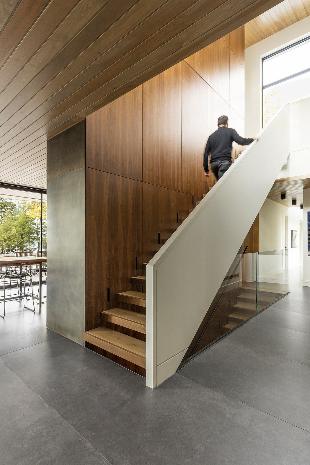 Elegant wooden staircase with glass panels leads to upper level in modern interior.