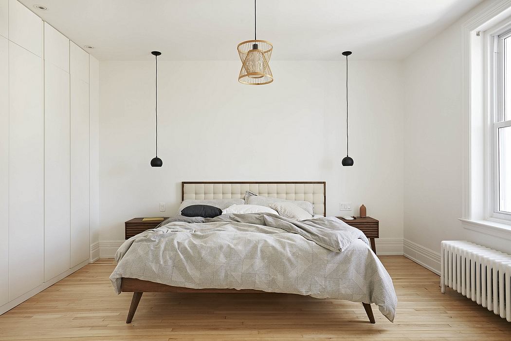 Cozy, minimalist bedroom with wooden furniture, pendant lights, and plush bedding.