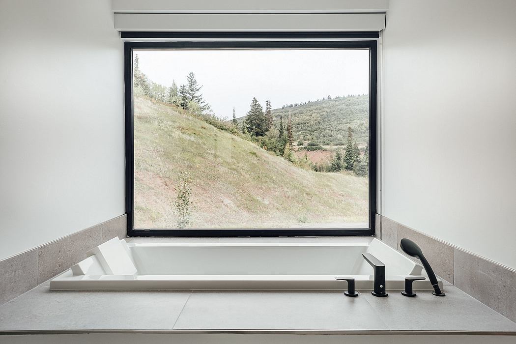Serene bathroom with modern tub, black fixtures, and panoramic mountain view through large window.