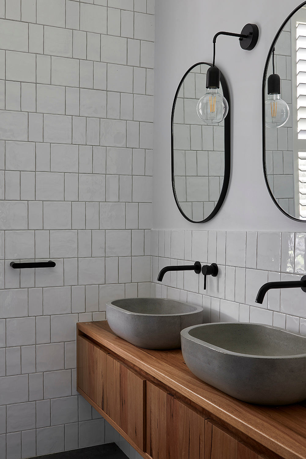 A modern bathroom with gray tile walls, a wooden vanity, and black fixtures.