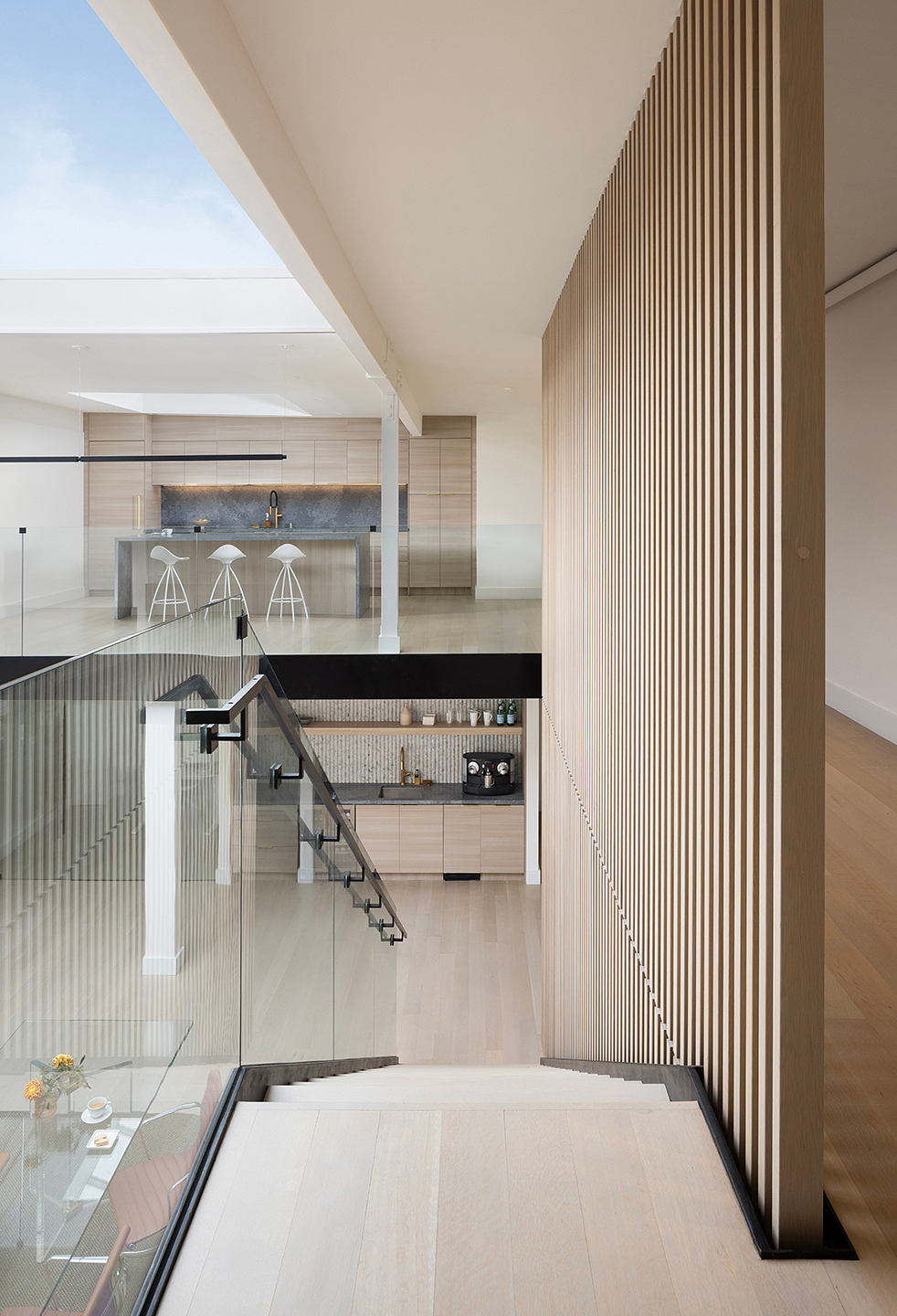 Modern open-concept interior with wood paneled walls, glass staircase, and kitchen.