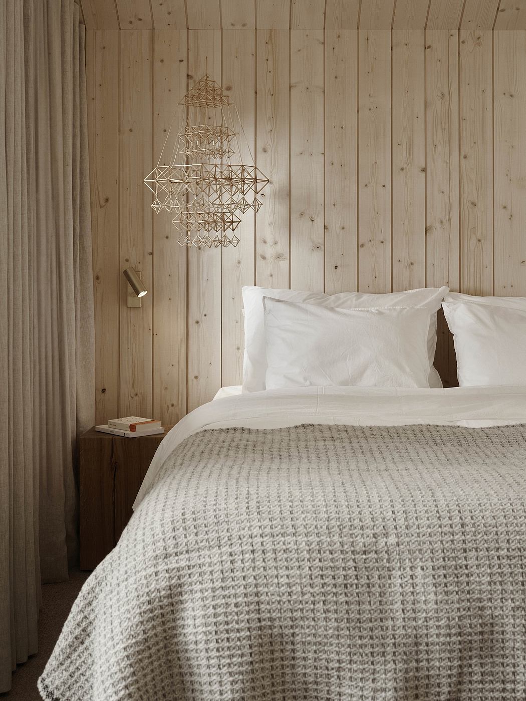 A cozy bedroom with a wooden paneled wall, a modern geometric light fixture, and a knitted throw.