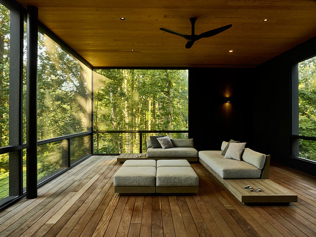 Cozy, modern living space with expansive glass walls overlooking lush forest.